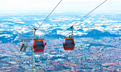 Red gondola ski lift with a city landscape and mountain view in the background, located at Maribor Ski Resort. A popular ski holiday destination in Slovenia. © Praewphan