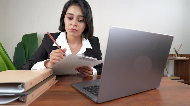 Close up of confused young working business woman boss manager employee sits on chair at workspace desk hold project paper examine online information on laptop feels confusion with serious face.