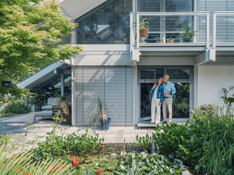 Married couple standing happily in modern house garden in summer