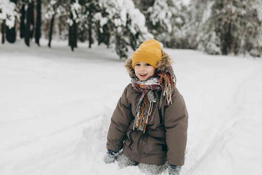 Happy child in winter clothing smiling while playing in snow outdoors