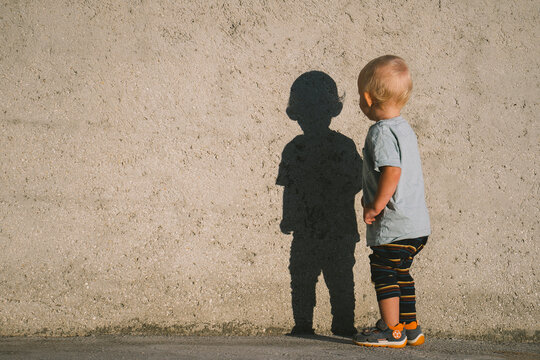 Child in casual clothes observing his shadow on a wall outdoors