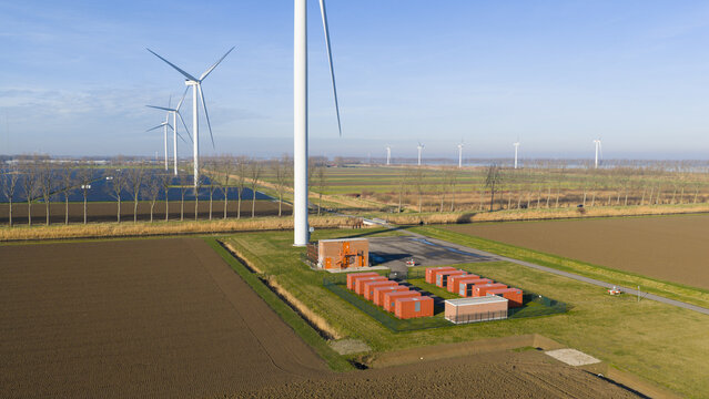 Aerial view of wind turbines and battery storage units set against a backdrop of bare fields under a clear sky, Middelharnis, South Holland, Netherlands.