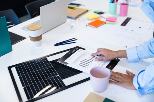 Office workplace with solar panel sample and hand analyzing energy chart