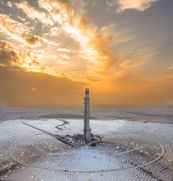 Aerial view of a solar power tower piercing the horizon under a sky ablaze with fiery hues, a monument in the desert landscape, Ashalim, South District, Israel.