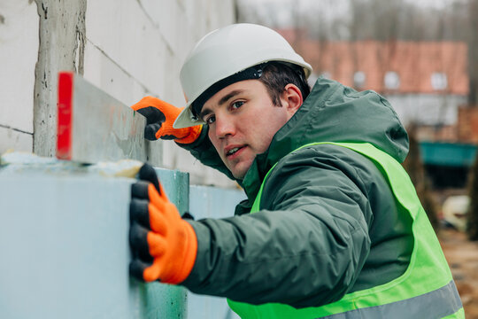 Builder checking wall insulation with level at construction site outdoors
