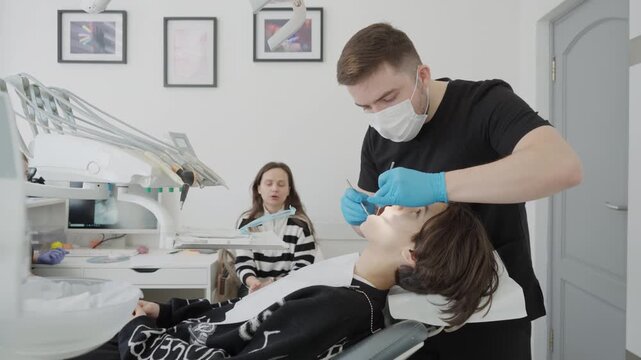Male doctor examines boy oral cavity and consults parent discussing treatment plan. Family visit to pediatric dentistry clinic includes medical advice communication and stomatology checkup.