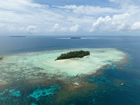Aerial view of the vibrant turquoise waters encircling Cemara Kecil Island, contrasting with the deep blues of the open sea, Karimunjawa, Central Java, Indonesia.