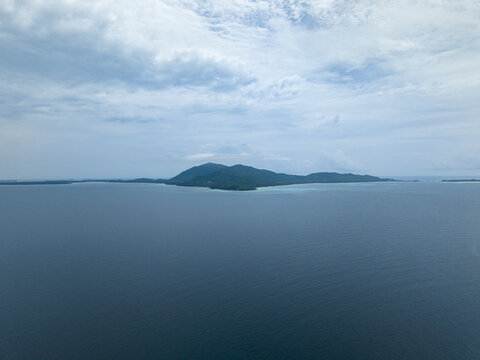 Aerial view of lush green island surrounded by deep blue waters under a serene sky, Cemara Kecil Island, Karimunjawa, Central Java, Indonesia.