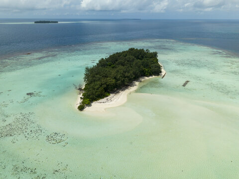 Aerial view of a lush island surrounded by shallow turquoise waters meeting the deep blue sea at the horizon, Karimunjawa, Central Java, Indonesia.