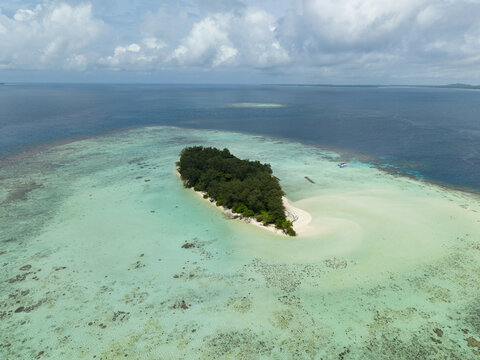 Aerial view of a lush, green island embraced by shallow turquoise waters, a serene escape under a vast sky, Karimunjawa, Central Java, Indonesia.
