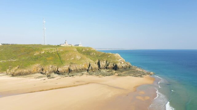 Aerial view of the scenic Cap de Carteret cliffs and sandy beach on a clear day in Normandy, France. The turquoise sea meets rugged rocks and a lighthouse atop the headland.