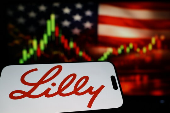 Kiel, Germany - 03-03-2026: US pharmaceutical company Eli Lilly and Company logo on smartphone against US flag and rising stock market candlestick chart concept