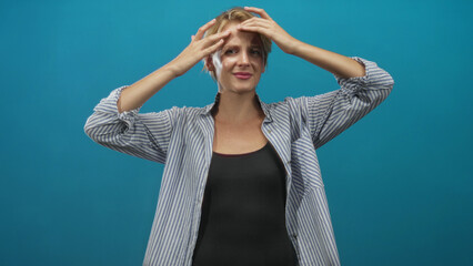 Woman pressing hands to forehead and massaging temples in a blue studio, striped shirt visible and eyes closed; relief wellness.