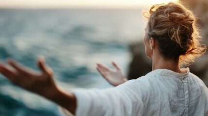 Fototapeta premium A woman stands atop a cliff with arms open wide, embracing the vast ocean view at sunset, representing freedom, connection, and the beauty of nature.