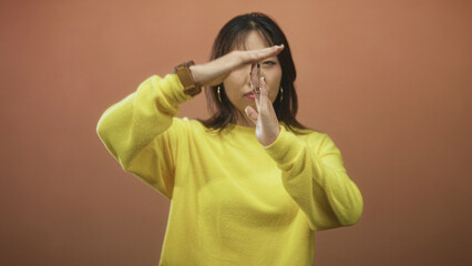 Young chinese woman in yellow sweater holds finger to lips for silence with hand near mouth and hoop earring visible in studio  silence introspection. © Krakenimages.com