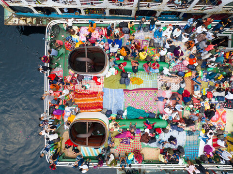 Aerial view of vibrant crowds gather atop a ferry, their colorful clothes and mats contrasting against the dark water, Dhaka, Dhaka Division, Bangladesh.