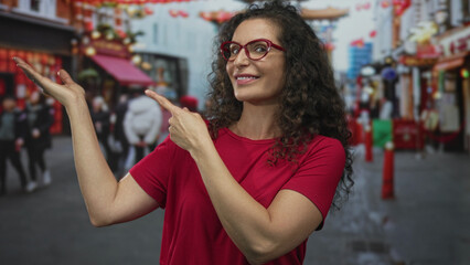 Fototapeta premium Woman wearing red glasses pointing finger at empty space on busy city street under daylight; curiosity.