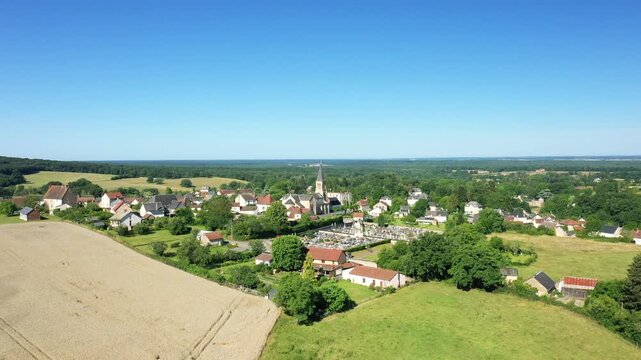 Drone shot of the rural village of Saint Honore les Bains surrounded by fields and greenery under a clear blue sky.
