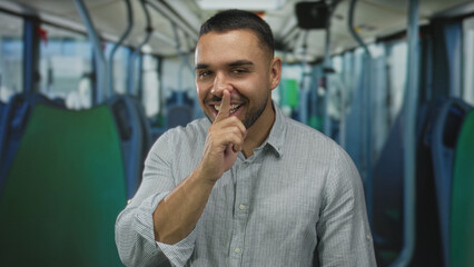 Young hispanic man standing upright on bus points finger to lips while making direct eye contact on street  secrecy caution privacy confidentiality. © Krakenimages.com