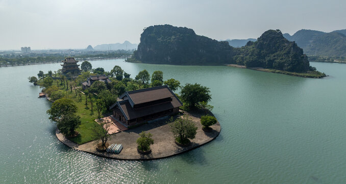 An aerial view of a beautiful Chua Vang  temple complex situated on an island in a tranquil lake, framed by dramatic karst mountains. Ninh Binh, Vietnam.
