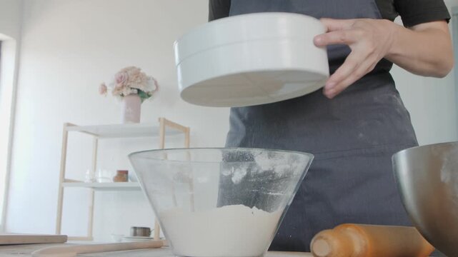 Female baker sifting flour for dough preparation