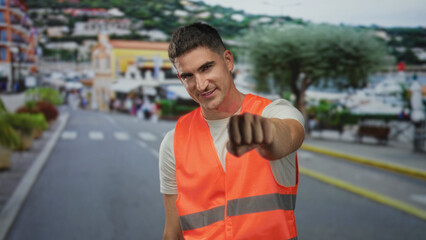 Man engineer in orange safety vest and white t shirt with clenched fist to chest on busy city...