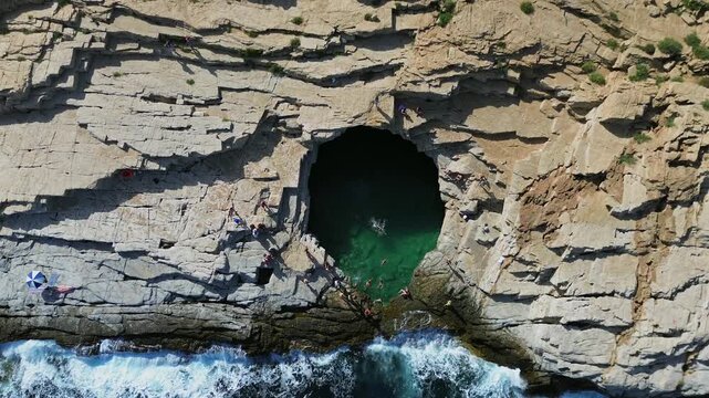 Cinematic drone ascent from the emerald waters of Giola natural sea pool revealing the rugged white limestone cliffs and the deep blue Aegean sea in a high contrast aerial view