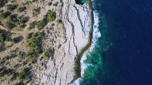 Cinematic top down drone view of the unique Giola natural sea lagoon in Thassos Greece featuring vibrant emerald waters against white limestone rocks and deep blue ocean waves.