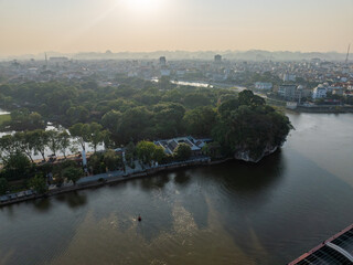Naklejka premium Aerial view of Ninh Binh City, Vietnam, featuring the River Day, Non Nuoc Pagoda, and distant karst mountains under a hazy sky.