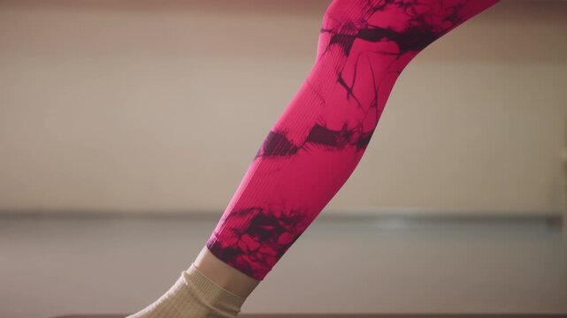 woman on mat in pink leggings performing ankle stretch with wool socks, focused balance and controlled breathing, morning home studio light, slow mobility routine for flexibility and joint care