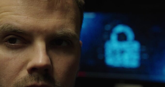 Intense close-up of a man&rsquo;s face with a blurred digital padlock on a computer screen in the background, representing cybersecurity, data protection, and online security threats.