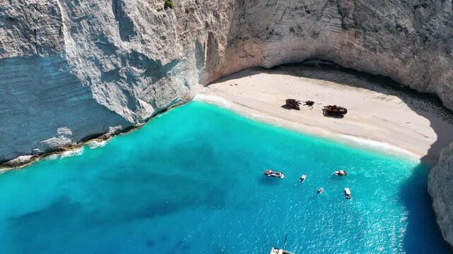 Aerial drone view of famous Navagio Shipwreck Beach with turquoise sea water and boats in Zakynthos island, Greece on a bright sunny da