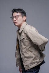 Obraz premium Asian man suffering from lower back pain holding lumbar area, spine injury and muscle strain concept, healthcare problem, tired male with glasses feeling discomfort, studio portrait isolated backgroun