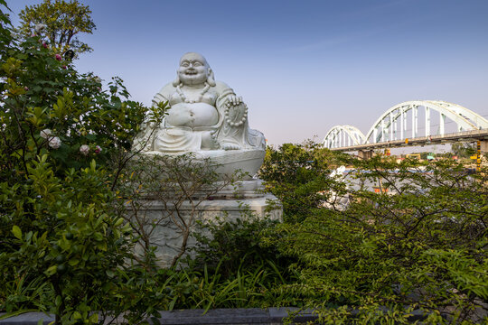 A statue of Budai, the laughing Buddha, sits in a garden at Non Nuoc Pagoda near the rail bridge in  Ninh Binh, Vietnam.