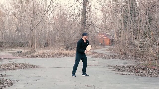 Active man in black sportswear playing paddle ball in a desolate park setting