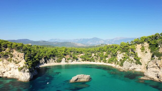 Scenic aerial shot of Alonaki Fanariou beach with turquoise water, rocky cliffs, and lush green forest under a clear blue sky in Greece.
