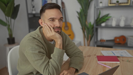 Fototapeta premium Young man thinking in cozy living room with guitar and plants surrounding him at home office setup