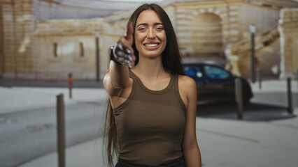 Fototapeta premium Woman extends right hand for handshake on city street near parked car and stone building, smiling with closed eyes; welcoming greeting.