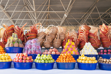 Vibrant outdoor fruit market stall with colorful piles of fresh pomegranates, apples, oranges, pineapples in bowls and stacks of wicker baskets. Samarkand Siab oriental market, Uzbekistan.
