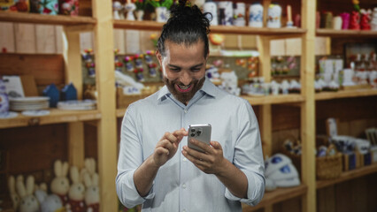 Obraz premium Man tapping smartphone with visible hands in a shop building stacked with home decor shelves, smiling and checking messages; joy connection.