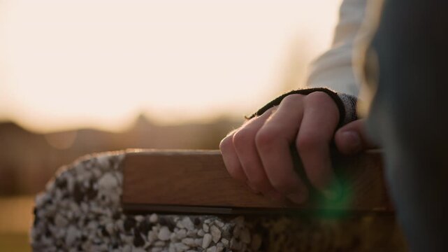 Guitarist at sunset. Serene musician enjoying sunset glow. Calm guitarist with bead bracelet in warm evening light. Peaceful musician resting hand on bench with glowing bokeh during sunset