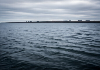 Obraz premium A serene and calm body of water under a cloudy sky with a distant landmass.