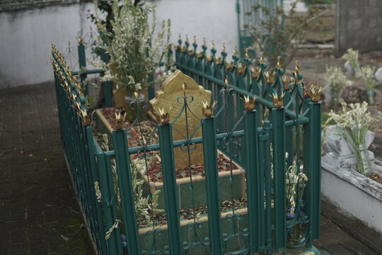 A traditional Muslim grave with a golden headstone and green iron fence decorated with flowers.