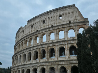 Fototapeta premium Ancient Roman Colosseum exterior with stone arches and classical statues, iconic Flavian Amphitheatre landmark under overcast sky, Rome, Italy