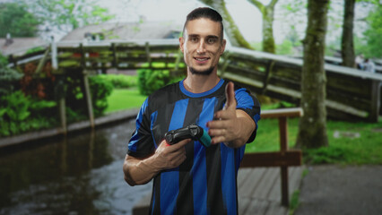 Man in blue striped shirt holding a gamepad and extending his right hand for a handshake in a forest  friendly sportsmanship. © Krakenimages.com