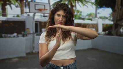 Woman with visible hands holds hands in timeout gesture on street basketball court wearing crop top...