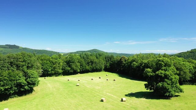 Aerial view of a sunny rural field with hay bales surrounded by lush green trees and rolling hills in the Morvan region, France.