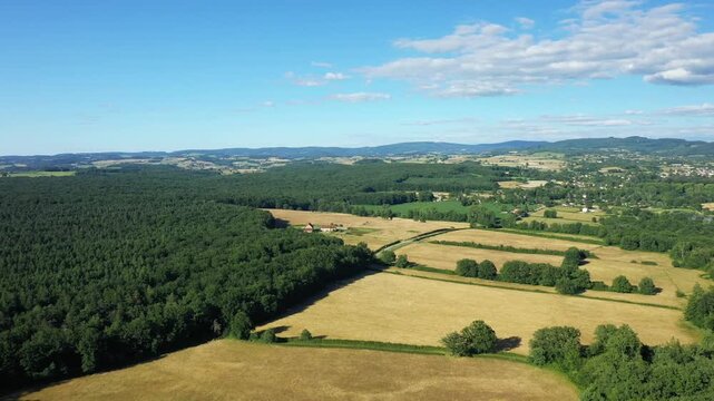 Scenic aerial view of patchwork fields, forests, and distant hills near Saint Honore les Bains, France, under a blue sky with scattered clouds.