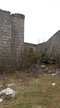 Abandoned Austro-Hungarian Golo Brdo fortress above Trebinje with distant hiker under heavy clouds. Conveys post-imperial military heritage, forgotten European strongholds, and Balkan frontier history