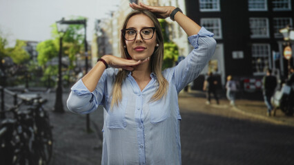 Fototapeta premium Woman framing face with hands on a street with bikes and blurred buildings, wearing glasses and pearl earrings; confidence.
